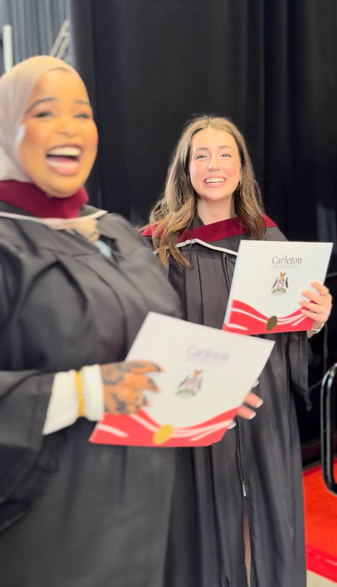 Two graduates smiling and holding their degree folders.