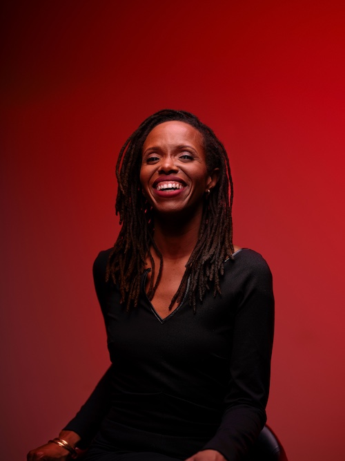 A headshot of Kellylee Evans wearing a black ress with a red background.