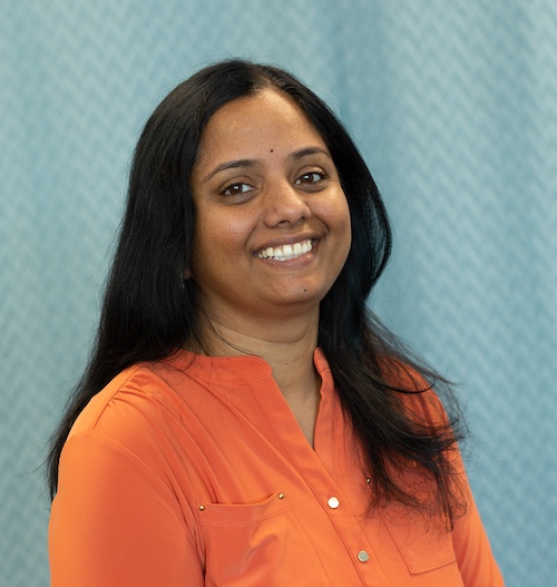 A headshot of Latha Vishnubhotla wearing an orange shirt with a blue background.